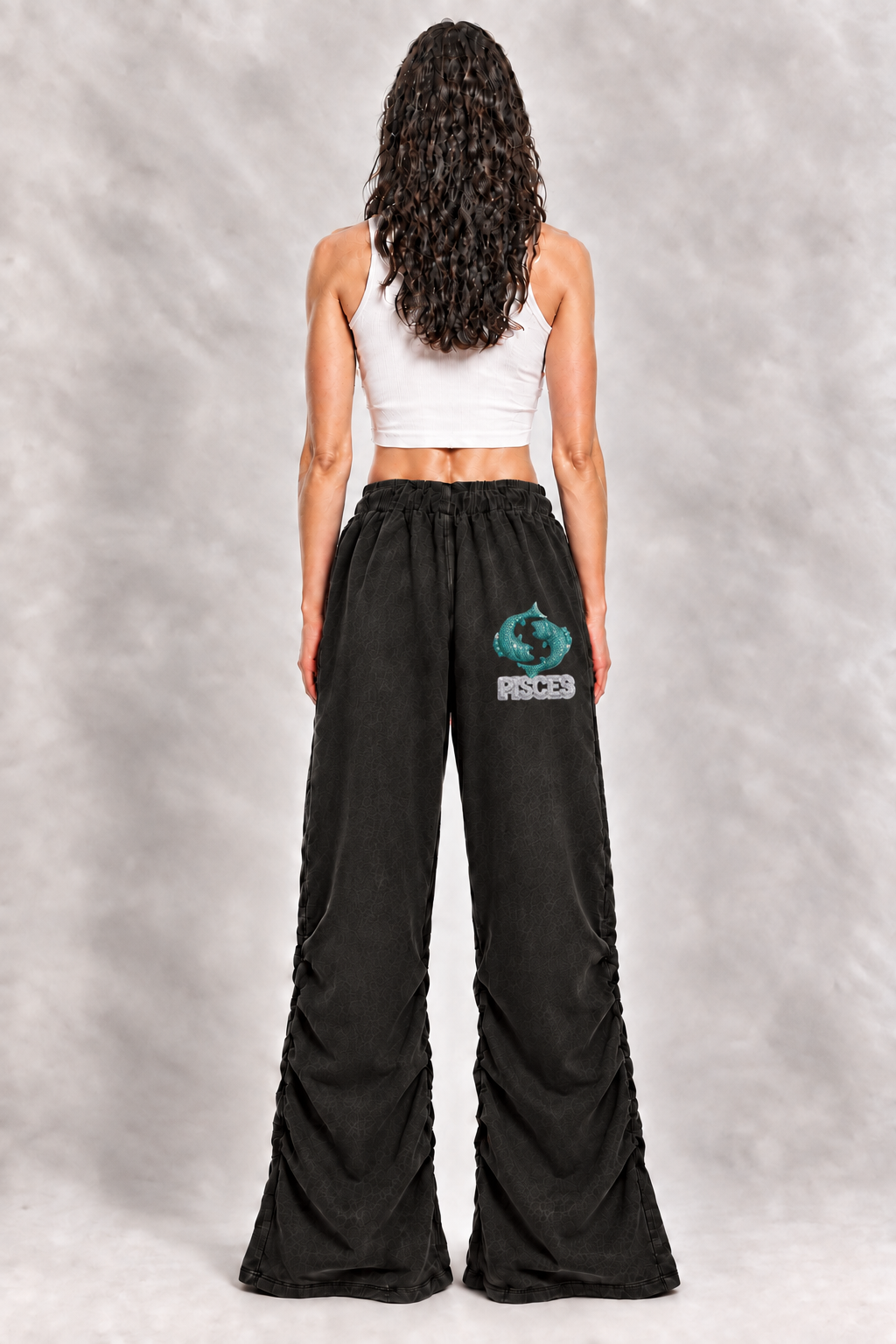 Female model wearing black Pisces vintage wash ruched sweatpants, back view; zodiac graphic and lettering are illustrative