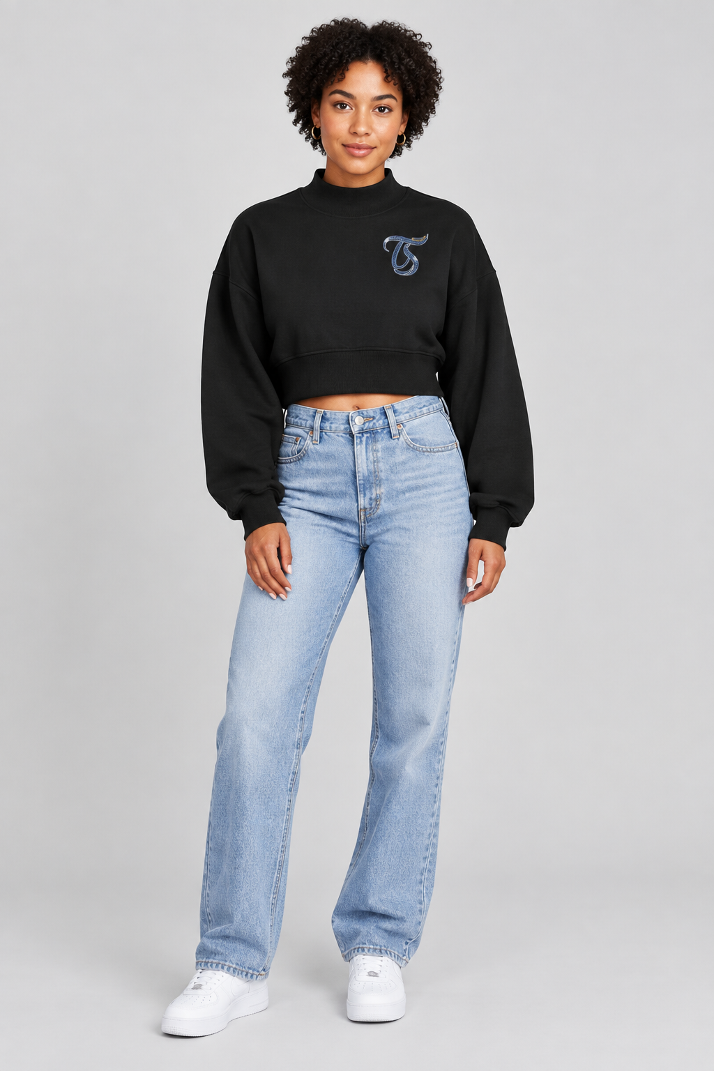 Female model in black Taurus women's crop mock neck sweatshirt, front with TS logo; illustrative print